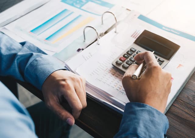 Mężczyzna w garniturze używa kalkulatora do obliczeń kosztów projektu.